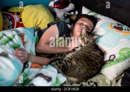 Il ragazzo di dieci anni dorme mentre il suo gatto tabby si anniora lui Foto Stock