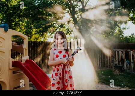 Giovane ragazza spray nebbia dal tubo da giardino in cortile Foto Stock