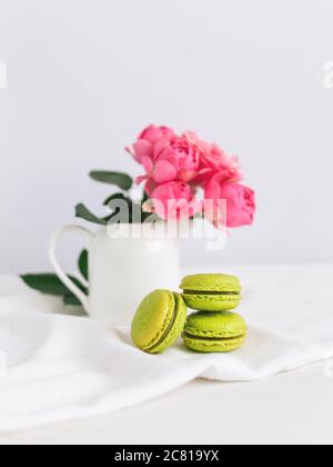 Tre gustosi macaron francesi e un vasetto con belle rose su sfondo bianco. Foto Stock