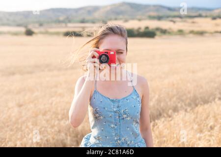 Sorridente giovane ragazza sul campo scattando foto al tramonto Foto Stock