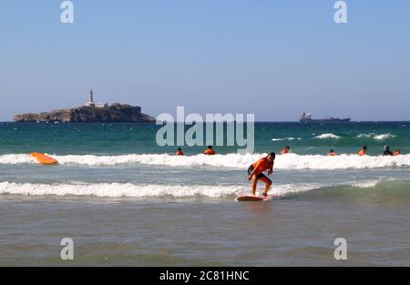 Giovane donna surf con l'isola delle corone e una nave ancorata in lontananza Santander Cantabria Spagna Foto Stock