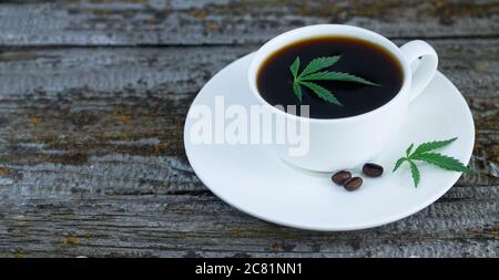 Tazza di caffè DI CANNABIS con foglie di canapa e chicchi di caffè arrostiti su un rustico tavolo di legno Foto Stock