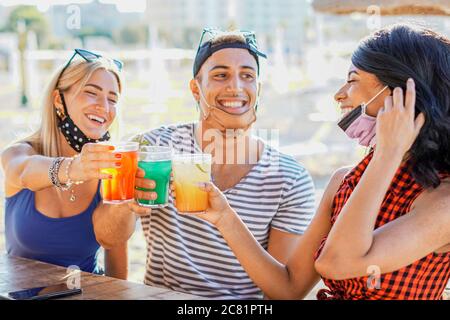 Persone che hanno una festa in spiaggia con maschera viso - giovani bere cocktail in tempo di coronavirus - amici divertirsi al bar - nuovo stile di vita conc Foto Stock