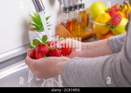 Donna mani lavando fragole in cucina. Mangiare frutta fresca e sana concetto. Primo piano Foto Stock