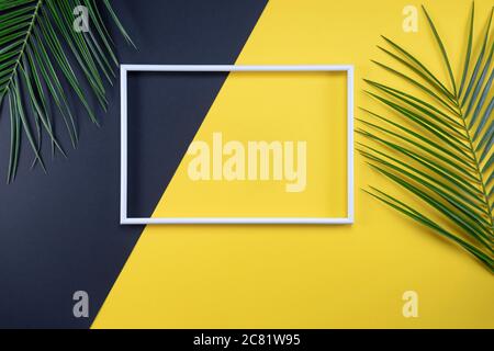 Composizione estiva con cornice fotografica e foglie verdi su sfondo giallo. Creazione di mockup con spazio di copia e foglie tropicali. Foto Stock