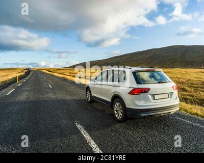 Un veicolo è parcheggiato sul lato di una strada asfaltata con una vista del vasto paesaggio nel sud dell'Islanda; Kjosarhreppur, regione meridionale, Islanda Foto Stock