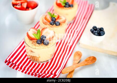 In casa, squisiti dessert Tiramisu' in vetri decorati con fragola, mirtillo, menta bianca sul tavolo di legno, Foto Stock