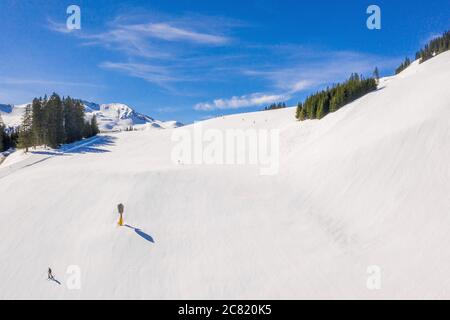 Area sciistica con sciatori che scivola sotto la pista innevata un cielo blu Foto Stock