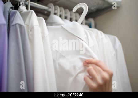 le camicie bianche da uomo sono appese sulle spalle dell'armadio Foto Stock
