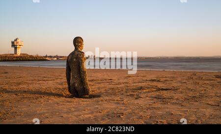 La luce dorata cade sulla spiaggia e un uomo di ferro prima del tramonto sulla spiaggia di Crosby vicino a Liverpool (Inghilterra) nel luglio 2020. Foto Stock