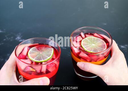 Mano dell'uomo e della donna che tiene un bicchiere di vino rosso Sangria fatto in casa su un tavolo di marmo nero Foto Stock