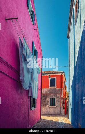 Isola di Burano stretta strada acciottolata tra case colorate edifici con pareti multicolore e biancheria da letto appesa su linea di vestiti, vista verticale, provincia di Venezia, Regione Veneto, Italia settentrionale Foto Stock