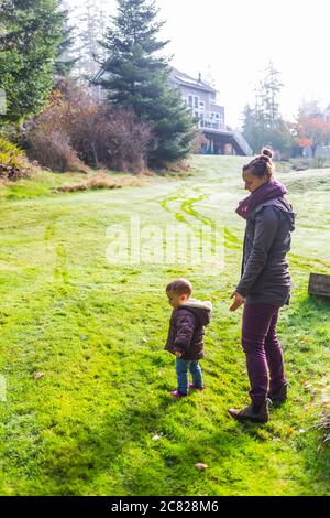 Madre con figlia giovane in erba in un cortile dietro una casa; Whidbey Island, Washington, Stati Uniti d'America Foto Stock