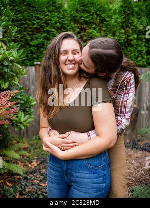 Un giovane uomo che tiene la sua ragazza in un abbraccio e la bacia sulla guancia; Bothell, Washington, Stati Uniti d'America Foto Stock