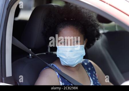 Donna afroamericana seduta in auto indossando maschera monouso Foto Stock