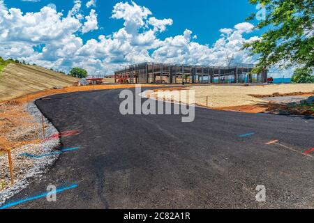 Ripresa orizzontale di una nuova strada coperta di nero che conduce a un cantiere commerciale. Foto Stock