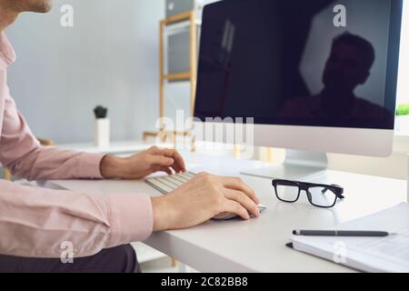 Crop anonimo dipendente maschile che lavora su computer desktop in ufficio Foto Stock