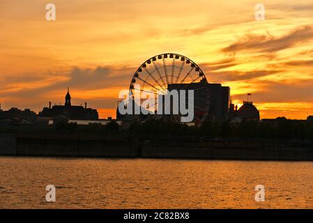 Ruota panoramica di Montreal nel porto vecchio al tramonto. Riflessi di raggi solari sul fiume Saint Laurent. Foto Stock