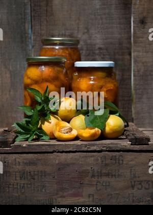 Vasi di marmellata di albicocche con menta su una vecchia scatola di legno su sfondo di legno intemperato Foto Stock