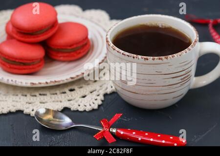 Una tazza di caffè su sfondo scuro con amaretti di color corallo Foto Stock