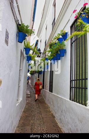 Cordoba, Spagna - 02 settembre 2015: Una donna in abito rosso che cammina attraverso la strada stretta con vasi di fiori durante il festival patio appeso sulla wa bianca Foto Stock