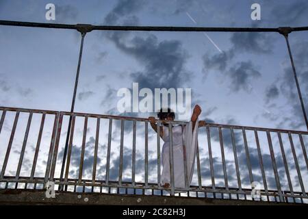 Un attraente modello femminile si pone su una recinzione dal sentiero di un ponte. Foto Stock