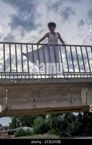 Un attraente modello femminile si pone su una recinzione dal sentiero di un ponte. Foto Stock