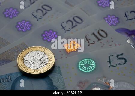 Monete inglesi da una sterlina in cima alle nuove banconote in polimero con simbolo visibile della sterlina e ologramma, Foto Stock