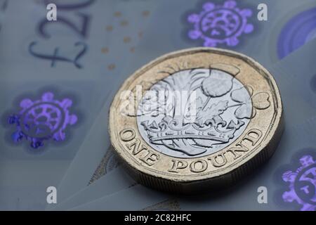 Monete inglesi da una sterlina in cima alle nuove banconote in polimero con simbolo visibile della sterlina e ologramma, Foto Stock