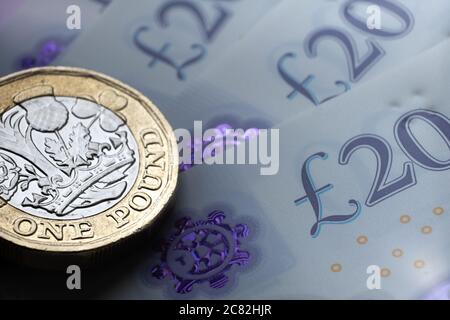 Monete inglesi da una sterlina in cima alle nuove banconote in polimero con simbolo visibile della sterlina e ologramma, Foto Stock