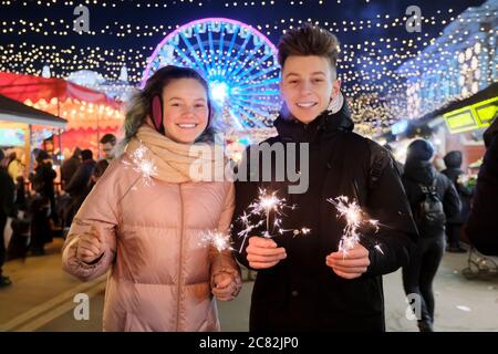 Felice coppia adolescente con sparklers che festeggia e divertirsi al mercato di Natale Foto Stock