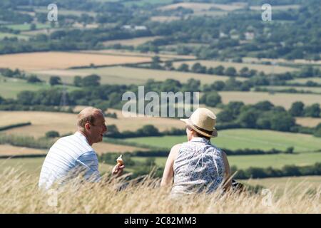 Coppia di mezza età seduta su una collina a Devil's Dyke Valley, South Downs, Sussex, UK, mangiare gelato e parlare Foto Stock