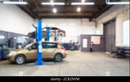 Interni in officina per riparazioni auto in bokeh, sfondo sfocato sfocato. Auto su ascensore in officina meccanica o garage, veicoli interni manutenzione. Luogo di lavoro A. Foto Stock