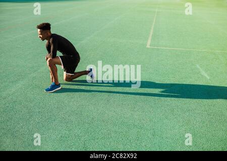 Vista laterale del giovane sportivo afroamericano sul campo di calcio allo stadio Foto Stock
