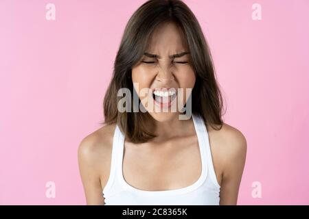 Giovane donna frustrata con gli occhi chiusi e la bocca aperta su fondo rosa chiaro Foto Stock