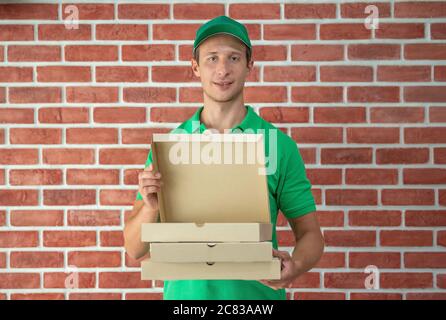 Addetto alla consegna in T-shirt con cappuccio verde pronto per l'invio della scatola di consegna degli alimenti di fronte all'ufficio personalizzato. Concetto di consegna e shopping online. Foto Stock