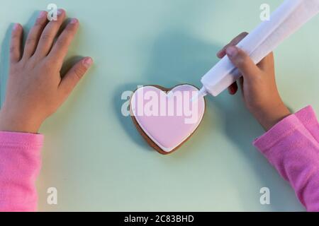 Bambina che decora i biscotti. Mani e biscotti del bambino coperti con smalto colorato. Dolci fatti in casa. Cucinare con i bambini. Presentare per gli amici Foto Stock