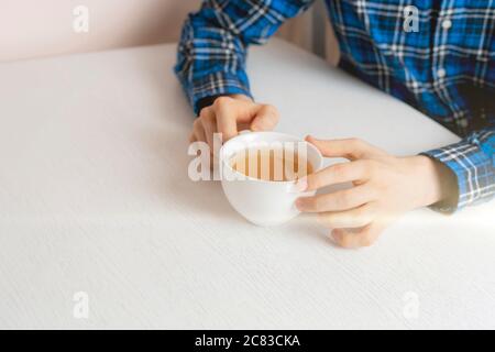 una persona seduta al tavolo e beve una tazza di tè a casa la sera Foto Stock