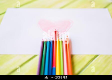 Primo piano di un disegno a cuore rosso su un bianco carta con matite colorate sul tavolo Foto Stock