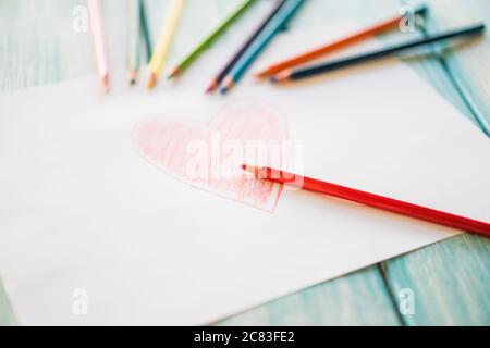 Primo piano di un disegno a cuore rosso su un bianco carta con matite colorate sul tavolo Foto Stock