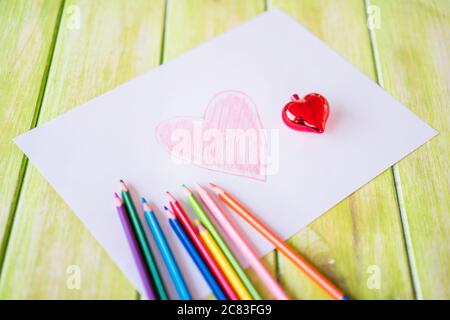 Primo piano di un disegno a cuore rosso su un bianco carta con matite colorate sul tavolo Foto Stock