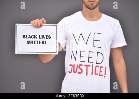 L'uomo sta tenendo carta con parole Black Lives materia davanti alla parete grigia. Foto Stock