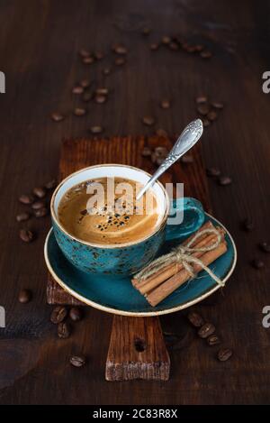 Il caffè nero in una tazza blu vintage e i chicchi di caffè sparsi sul vecchio tagliere scuro sono su un tavolo di legno marrone scuro, con spazio di copia Foto Stock