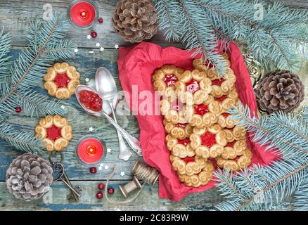 Composizione natalizia con biscotti dolci con marmellata, rami di abete e coni e la candela rossa bruciante sul vecchio tavolo di legno, vista dall'alto Foto Stock