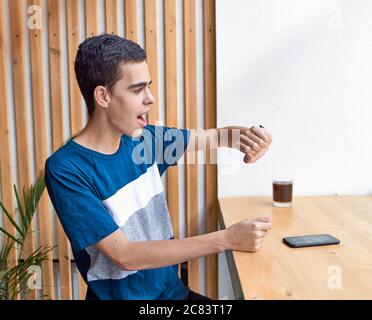 Un giovane adulto guarda l'orologio. Concetto di gestione del tempo. Uomo caucasico stressato con capelli neri che temono di arrivare in ritardo Foto Stock