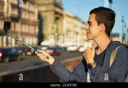 il giovane uomo con un telefono è sulla strada di una grande città e pollici su, blogger comunica con i popoli Foto Stock