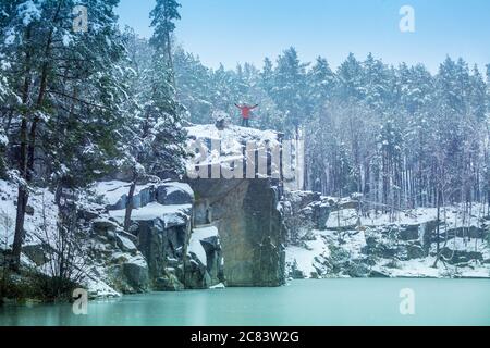 Un uomo rimane sul bordo della scogliera sul lungolago coperto di neve in inverno e guarda il lago bello Foto Stock