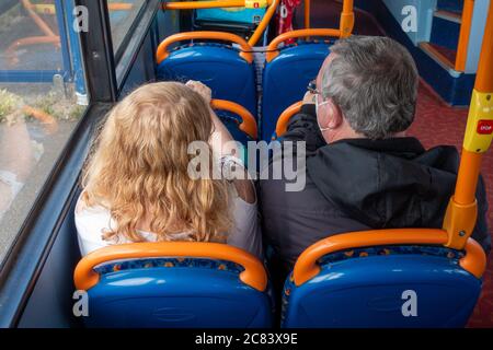 Una coppia che indossa maschere di faccia seduto su un viaggio in autobus seduto a parte durante le regole sociali di distanza Foto Stock