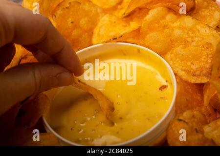 La ragazza prende un chip da un piatto rotondo con patatine e una pentola con salsa di formaggio al centro del piatto. Primo piano Foto Stock