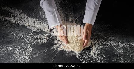 Chef o panettiere impastare un cumulo di pasta cruda su una superficie con farina sparsa in una vista dall'alto in basso sulle sue mani in un banner panoramico con copyspace Foto Stock